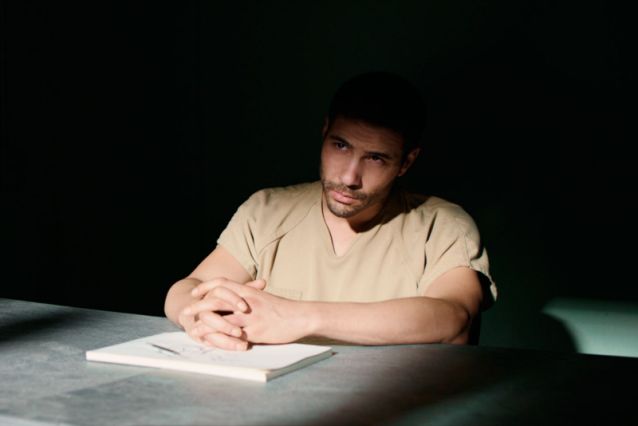 Tahir Rahim sitting in a dark interrogation room as seen in The Mauritanian.