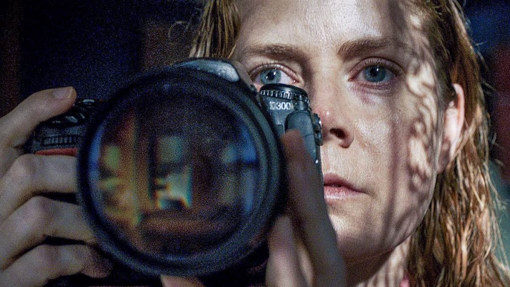 Amy Adams spying on her neighbors with a camera as seen in the new Netflix film The Woman in the Window.