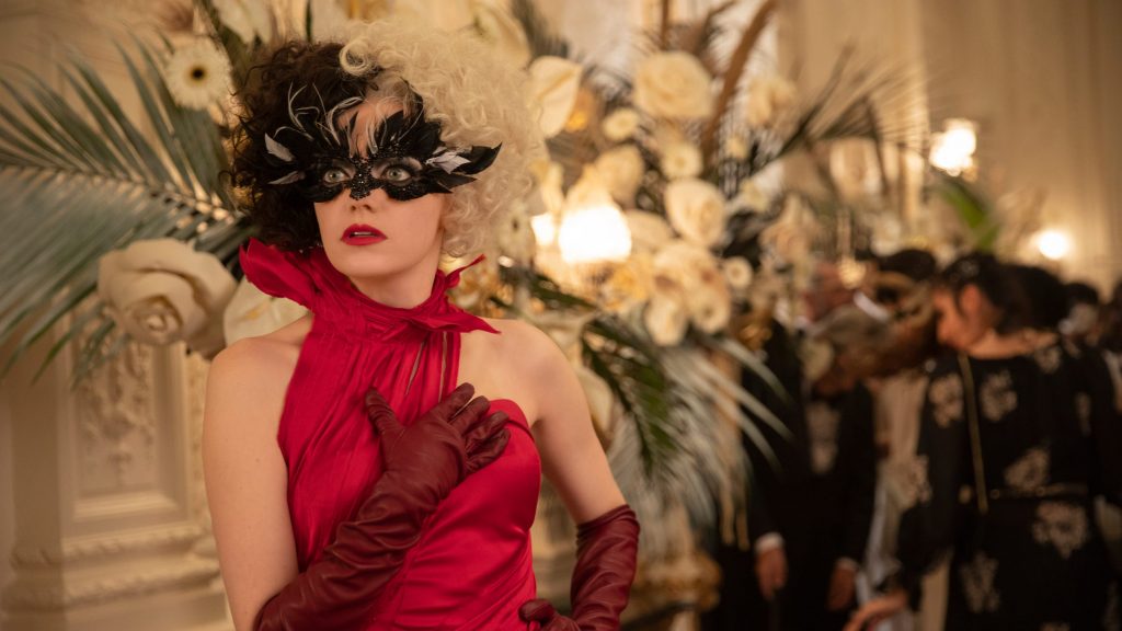 Emma Stone as Cruella posing in a red dress at a glamorous ball as seen in the new Disney live-action film.