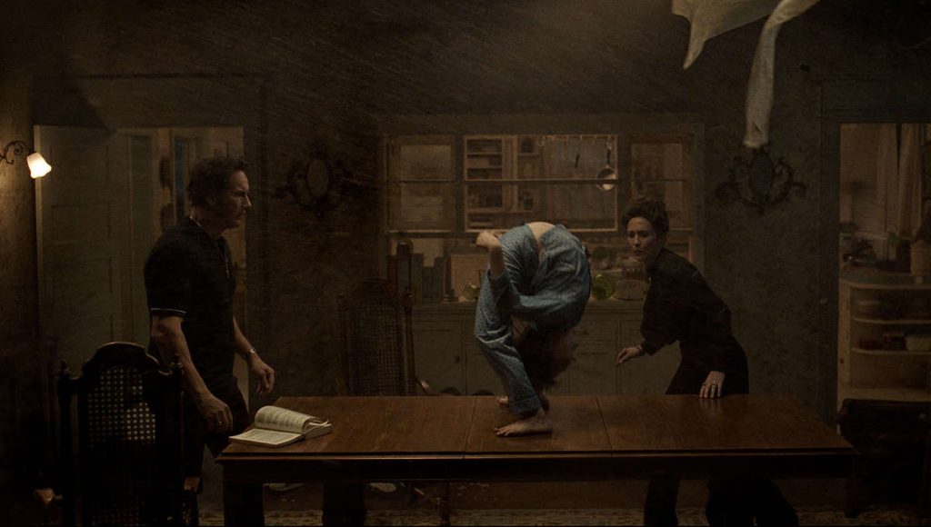 Patrick Wilson as Ed Warren and Vera Farmiga as Lorraine Warren performing an exorcism on a young boy as he bends over backwards on a table as seen in The Conjuring: The Devil Made Me Do It