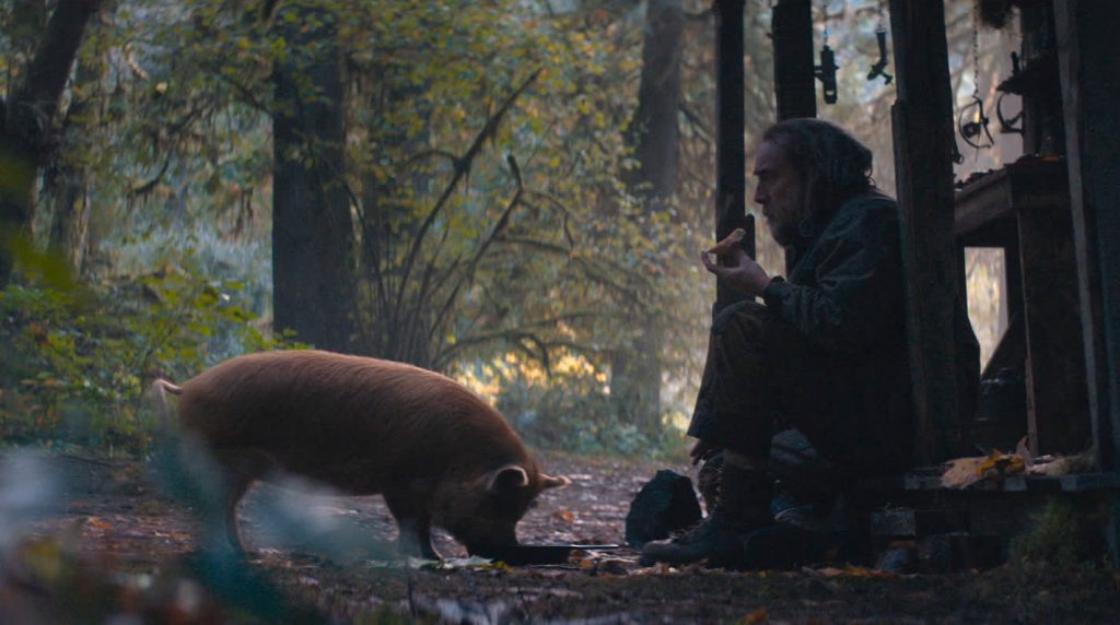 Nicolas Cage sits with his red pig while eating cooked truffles in the forest as seen in the new revenge drama PIG.