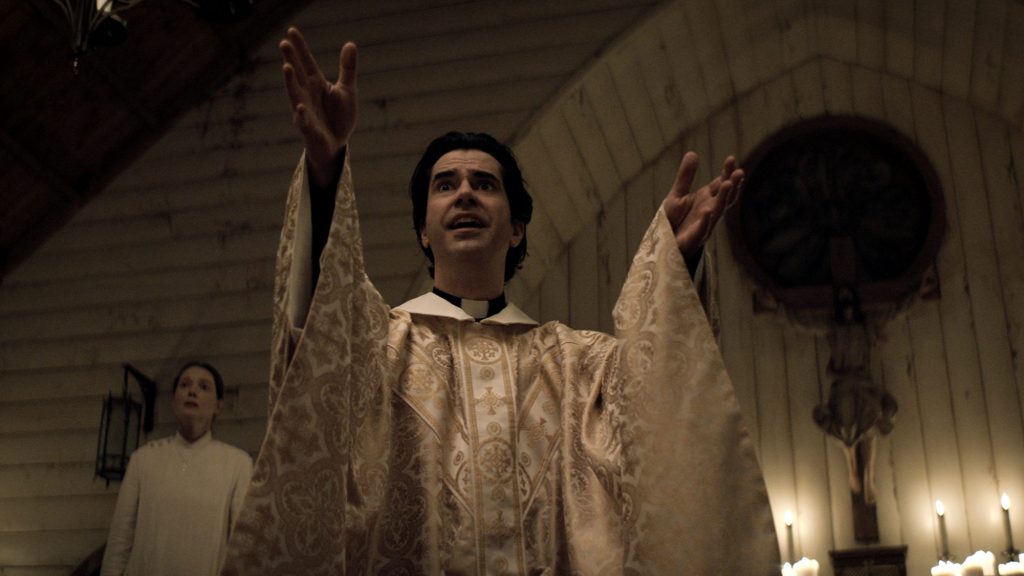 Samantha Sloyan as Bev Keane and Hamish Linklater as Father Paul lead a soulful sermon inside an old church as seen in MIDNIGHT MASS directed by Mike Flanagan on Netflix.