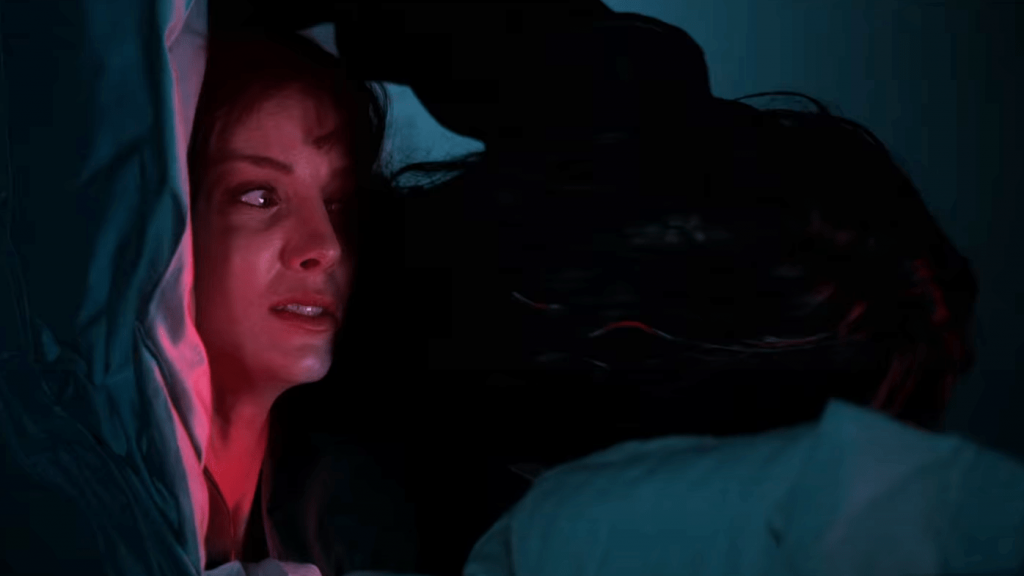 Annabelle Wallis laying down paralyzed under a bright red light as Gabriel the demonic killer creeps over as seen in MALIGNANT directed by James Wan.