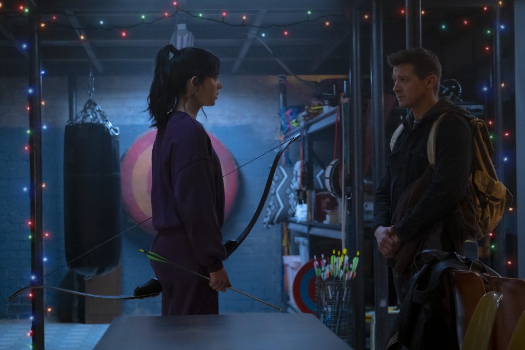Hailee Steinfeld as Kate Bishop and Jeremy Renner as Clint Barton meet in a room full of bow and arrow target practice as seen in the new Marvel series HAWKEYE on Disney+