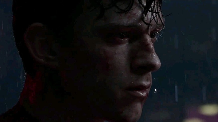 Tom Holland as Peter Parker holds back tears in pain as rain falls all over his face as seen in the Marvel Studios and Sony film SPIDER-MAN: NO WAY HOME.