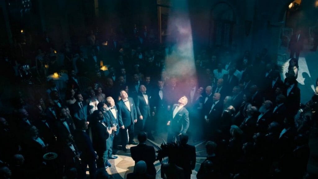 Daniel Craig as James Bond 007 caught in the middle of a spotlight while crashing a Spectre meeting as shot by cinematographer Linus Sandgren in NO TIME TO DIE.