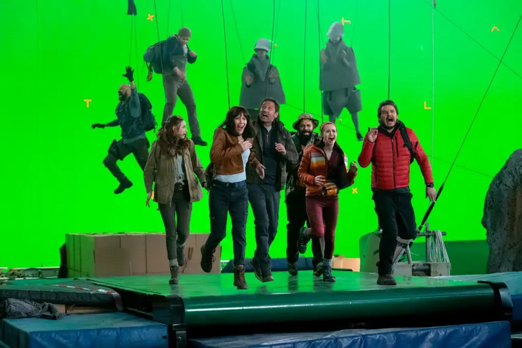 The main cast of THE BUBBLE pretend to run in fear on a large treadmill in front of a giant green screen while actors in digital reference dinosaur suits chase them on wires as seen in the new Netflix film directed by Judd Apatow.