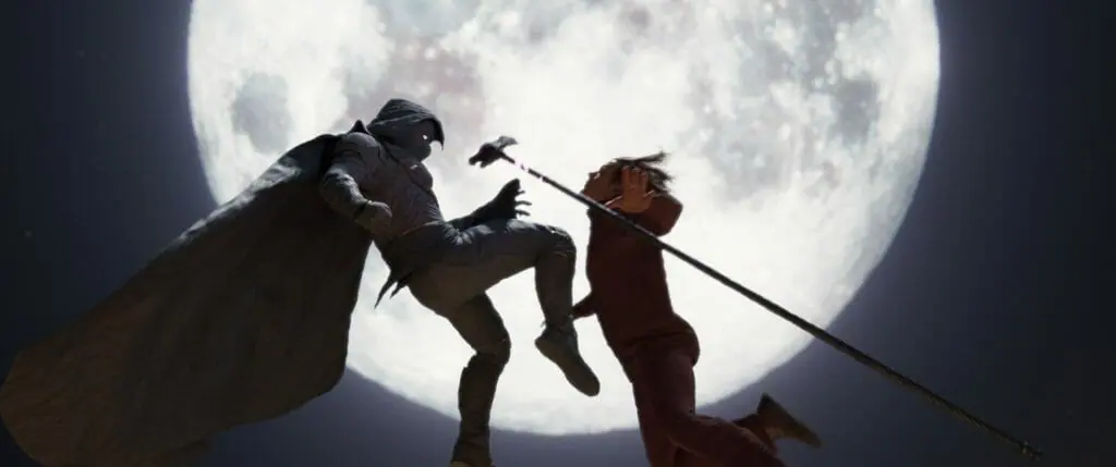 Moon Knight strikes an epic battle pose in front of a giant full moon as he knees Arthur Harrow in the face knocking him into the air as seen in the MCU Disney+ series written by Jeremy Slater.