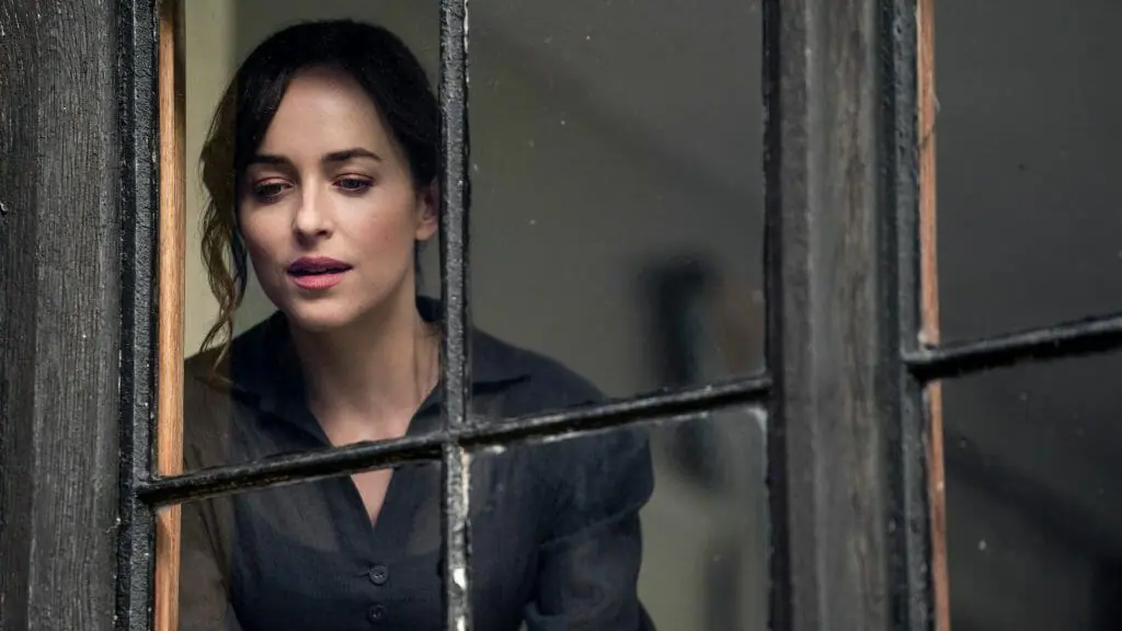 Dakota Johnson as Anne Elliot stares out of a large window in glee and wonder as seen in the 2022 Netflix adaptation of the classic Jane Austen novel PERSUASION.