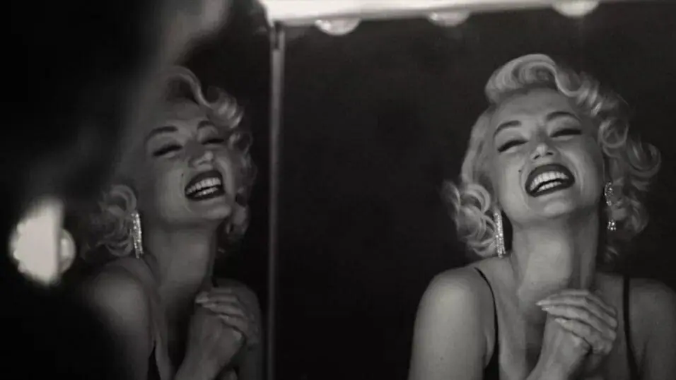 Ana de Armas smiles at her own dual reflection in the mirror as Marilyn Monroe in a tragic black and white shot from BLONDE.