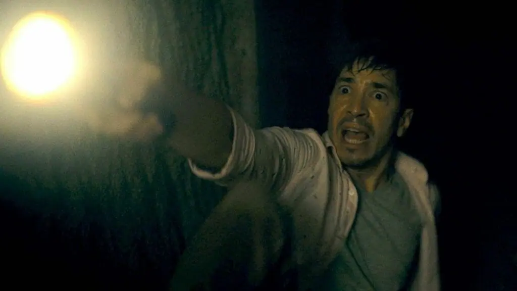 Justin Long crawls away from terror holding a flashlight in total fear while stuck underground in BARBARIAN coming to HBO Max in October 2022.