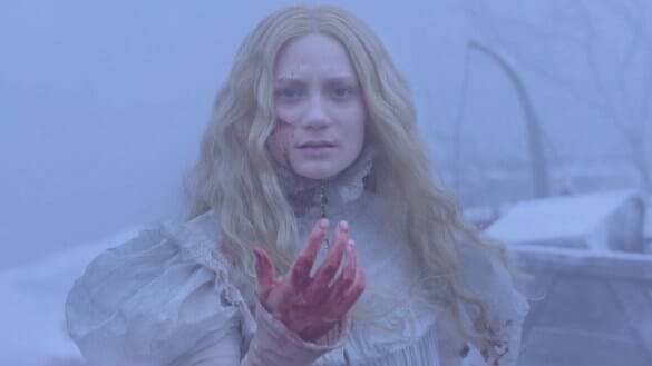 Mia Wasikowska with a bloody hand stands in the white snow of Crimson Peak.