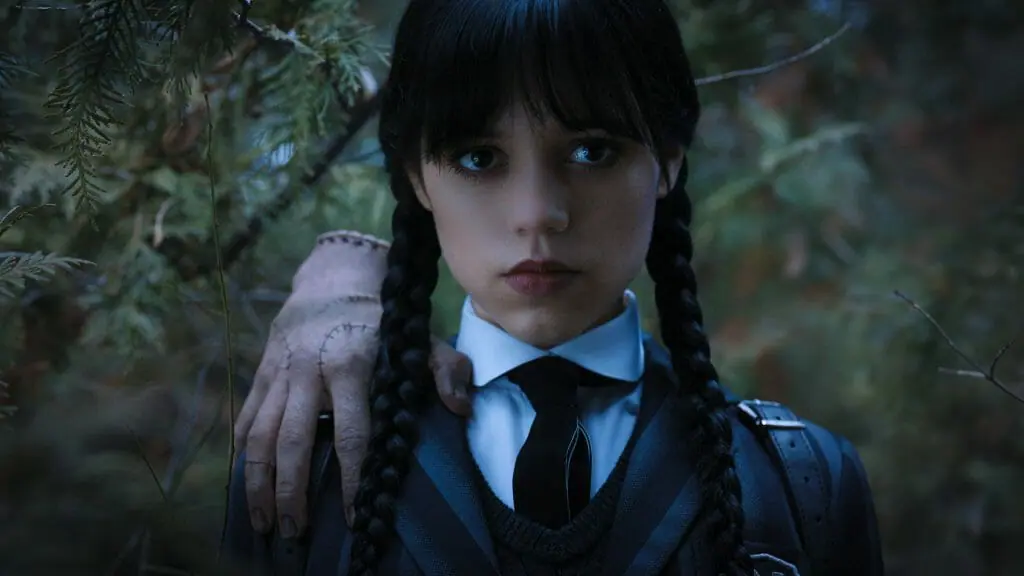 Jenna Ortega as Wednesday Addams strikes a brooding pose with the Thing severed hand on her shoulders in the new series coming to Netflix in November 2022.