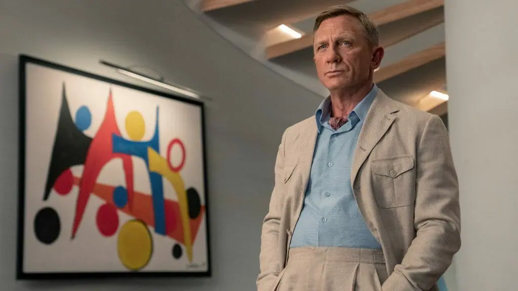 Daniel Craig stars as the great detective Benoit Blanc investigating a lavish tech billionaire mansion with fine colorful art over the walls in GLASS ONION: A KNIVES OUT MYSTERY on Netflix.