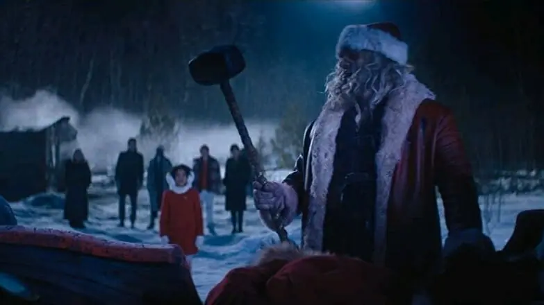 David Harbour as Santa Claus lifts up his ancient war hammer from his reindeer sleigh as a young girl played by Leah Brady watches in awe from behind in the Christmas action comedy VIOLENT NIGHT.