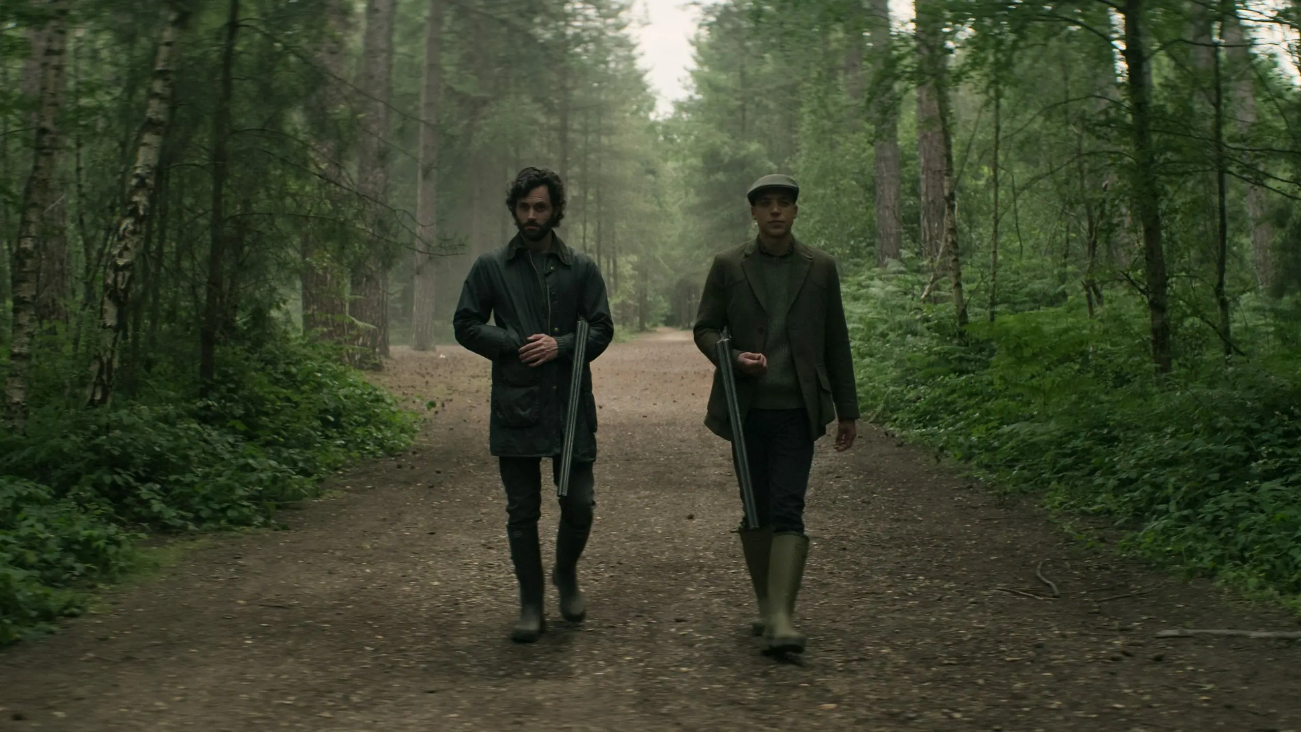 Penn Badgley as Joe Goldberg and Ben Wiggins as Roald Walker-Burton go hunting with old-school rifles in the British countryside in YOU Season 4 on Netflix.