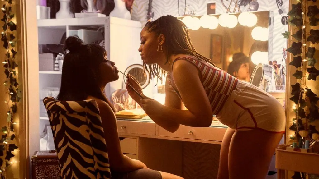 Dominique Fishback as Dre has her makeup done by Chloe Bailey as Marissa inside a bright dressing room in the Amazon Prime Original horror thriller series SWARM.