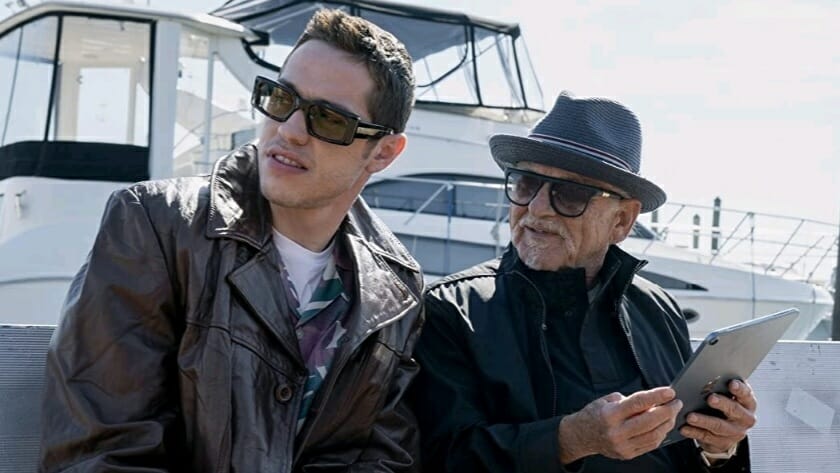 Pete Davidson stands next to his grandpa Poppy Davidson played by Joe Pesci on a boat dock while the two wear sunglasses in the Peacock original semi-autobiographical comedy series BUPKIS.