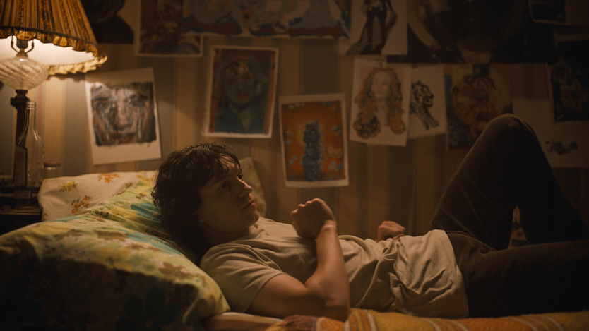 Tom Holland as Danny Sullivan lays down on the bed in his dimly lit room with his private colorful drawings all over the walls in THE CROWDED ROOM on Apple TV+.
