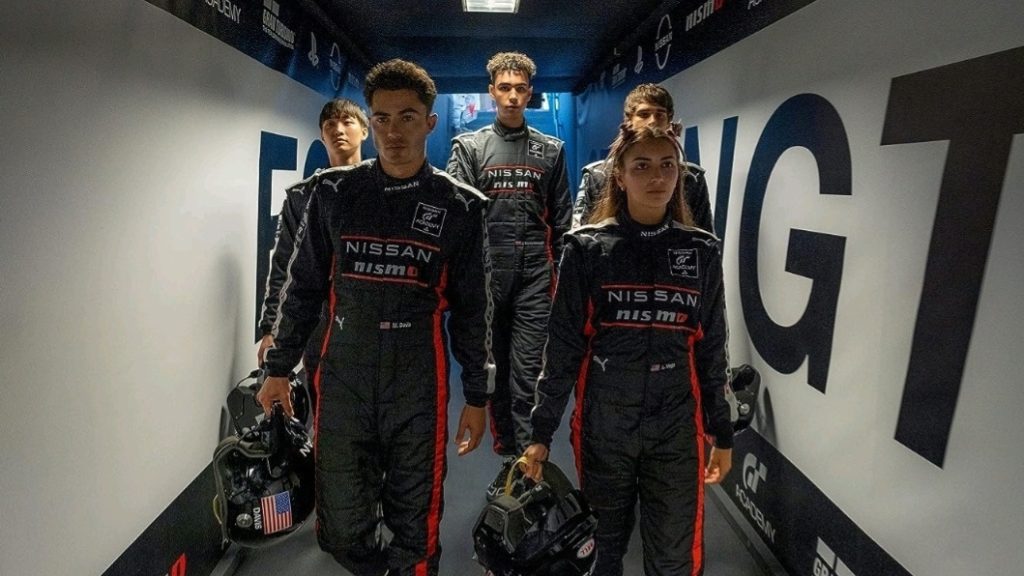 Sang Heon Lee, Josha Stradowski, Archie Madekwe, Darren Barnet, and Emelia Hartford walk down a hallway together in black Nissan GT uniforms in the GRAN TURISMO movie.