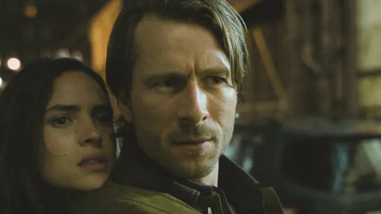 Adria Arjona and Glen Powell pose together in a cool action shot from the movie HIT MAN directed by Richard Linklater.