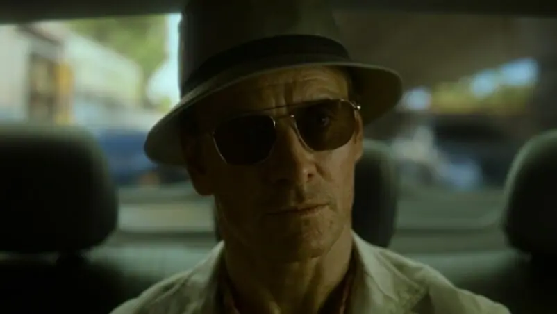 Michael Fassbender stars as the main unnamed assassin wearing a white bucket hat and sunglasses in THE KILLER directed by David Fincher on Netflix.