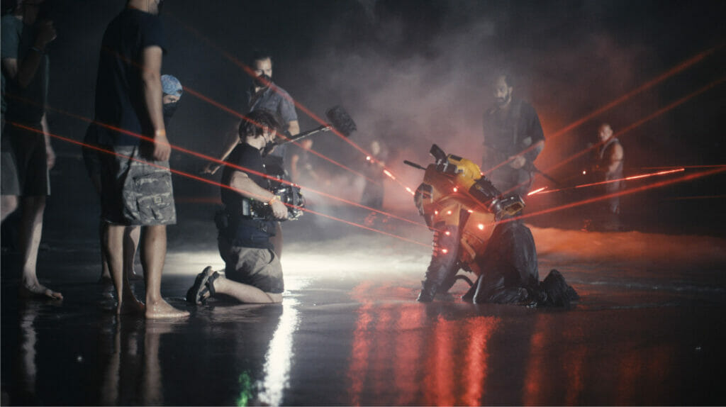 Director Gareth Edwards shoots a scene with actor John David Washington on a beach at night while he's in a hazmat suit surrounded by lasers on the set of THE CREATOR.