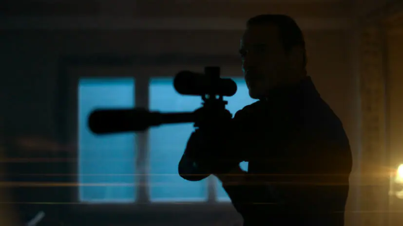 A dark silhouette of Michael Fassbender aiming a sniper rifle in the Netflix movie THE KILLER directed by David Fincher.