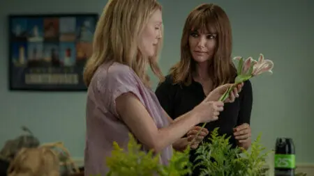Natalie Portman stares intensely at Julianne Moore while they both pick flowers in the romantic drama Netflix film MAY DECEMBER.