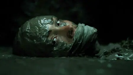 Natalie Alyn Lind stars as the character Norma raising her head out of a pool of mud with her mouth covered by a tied up cloth in PET SEMATARY: BLOODLINES streaming only on Paramount+.