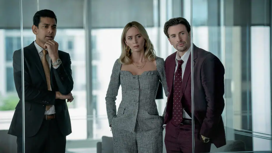 Amit Shah, Emily Blunt, and Chris Evans star as pharmaceutical sales reps in the middle of a tense meeting in their up-scale office in the Netflix original film PAIN HUSTLERS.