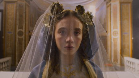 Sydney Sweeney has a dreadful look on her face while having her hair in regal buns under a white veil during a ritual scene in the religious horror film IMMACULATE.