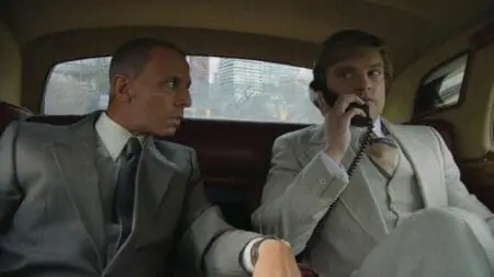 Roy Cohn played by Jeremy Strong looks over at young Donald Trump played by Sebastian Stan answering an important phone call while riding in the back of a limo in the biopic film THE APPRENTICE.