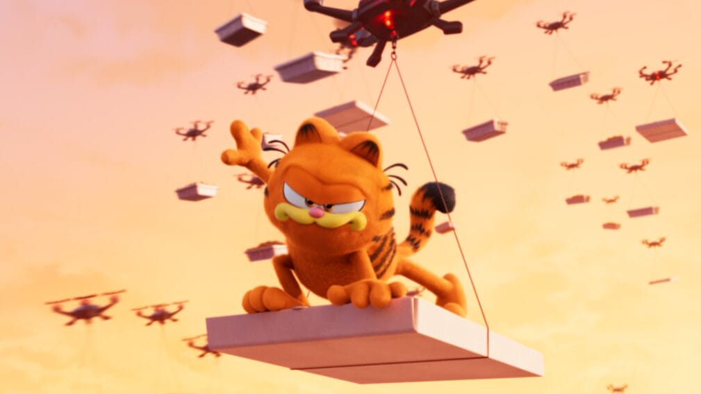 Garfield voiced by Chris Pratt rides a pizza box being carried by a delivery drone as hundreds of more drones follow behind him in the third act train chase scene from THE GARFIELD MOVIE.