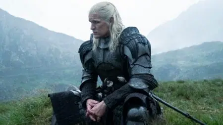 Matt Smith stars as Daemon Targaryen sitting in a huge green field wearing his black dragon armor in HOUSE OF THE DRAGON Season 2.