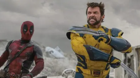 Wolverine played by Hugh Jackman shows off his adamantium claws in his comic accurate yellow and blue costume next to Deadpool played by Ryan Reynolds during an intense fight scene in in the MCU movie DEADPOOL & WOLVERINE.