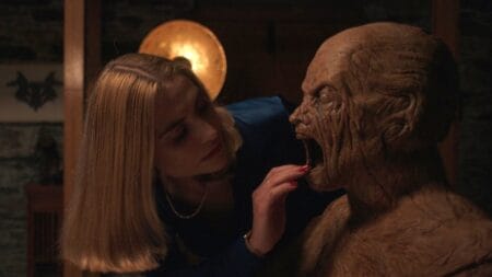 Caroline Menton looks into the open mouth of a scary life-size wooden man figure in the 2024 horror movie ODDITY.
