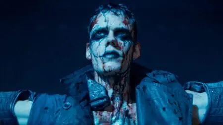 Bill Skarsgård as Eric Draven steps into a large spotlight on a theatre stage showing off his messy black makeup and blood-soaked costume in the 2024 reboot of THE CROW.