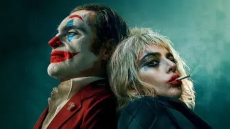 Joaquin Phoenix and Lady Gaga lean on each other's backs in their full respective clown makeup as the Joker and Harley Quinn in the sequel Joker Folie à Deux.