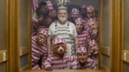Paddington Bear and a large group of prison inmates pose together happily in their pink striped uniforms in a hilarious shot from PADDINGTON 2, coming to the Prime Video streaming service in September 2024.