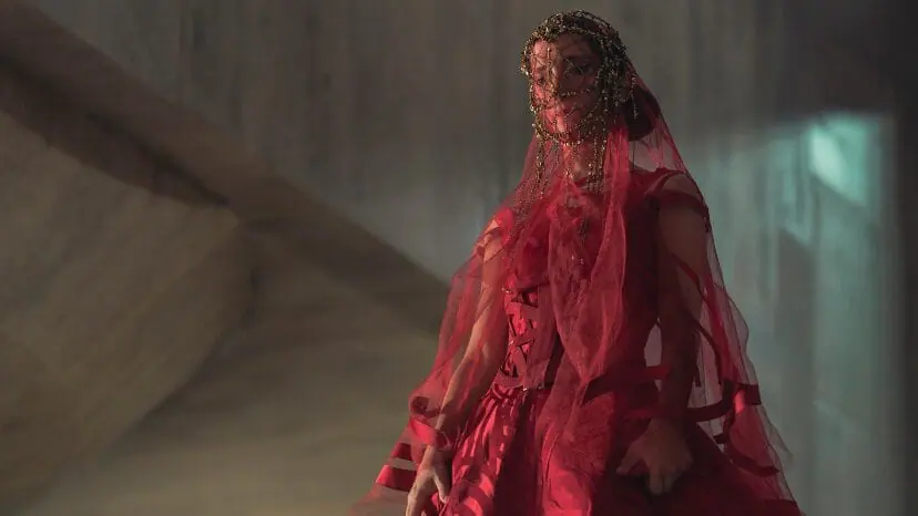 Sarah-Sofie Boussnina stars as Princess Ynez wearing a futuristic, lavish red wedding dress with a veil that covers her face in the HBO prequel series DUNE: PROPHECY. 