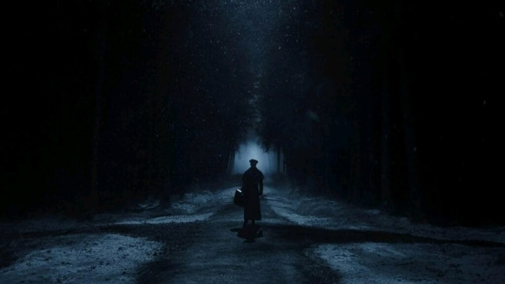 Thomas Hutter, played by Nicholas Hoult, walks down a lonely road in the middle of a gothic forest covered in snow in the NOSFERATU movie remake directed by Robert Eggers. 