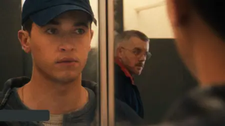 Tom Blyth looks into a restroom mirror and locks eyes passionately with actor Russell Tovey walking behind him into a stall in the gay coming out drama movie PLAINCLOTHES.