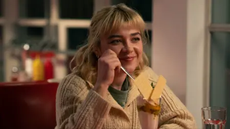 Florence Pugh shares a beautiful smile as she sits down in a British diner and enjoys a large milkshake in the A24 romance drama WE LIVE IN TIME, which is included in the complete Max February 2025 list of new films and TV shows.