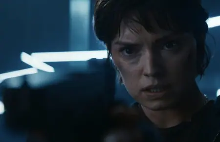 A close-up of Daisy Ridley showing off her new black hair in a pixie cut as she holds up a gun to the camera as the elite ex-soldier Joey Locke in the high-rise action thriller movie CLEANER.