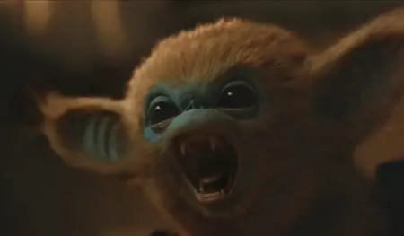 A small orange-furred and blue-faced Ochi with large eyes shows off its small black beady eyes and white fangs as it feels threatened in the A24 family fantasy adventure movie THE LEGEND OF OCHI.