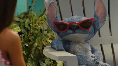 Stitch the small, adorable, and blue CGI alien looks cool while sporting red sunglasses and laying back on a lawn chair on the beach in the 2025 live-action remake of LILO & STITCH.