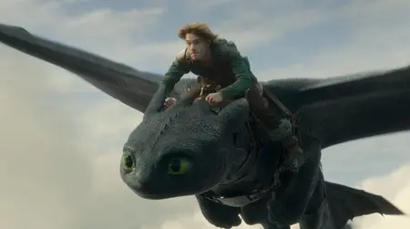 Mason Thames stars as the young boy Hiccup riding on top of the cute and large black dragon Toothless high in the sky surrounded by clouds in the 2025 live-action remake of HOW TO TRAIN YOUR DRAGON.