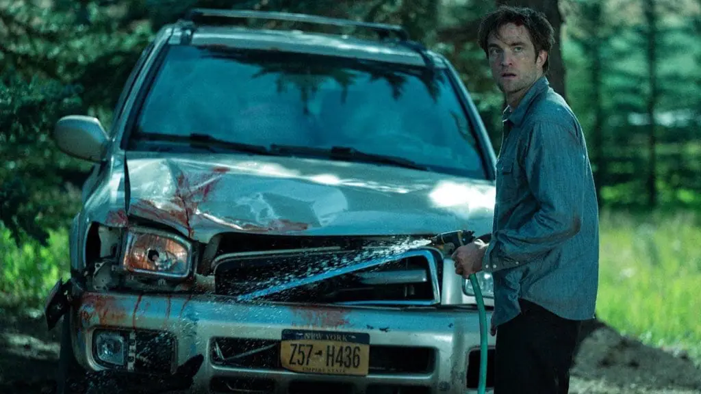 Robert Pattinson looks distressed as he tries to wash off blood from the front bumper of his damaged car in the psychological drama movie DIE, MY LOVE.