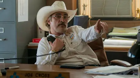 Joaquin Phoenix stars as the paranoid Sheriff Joe Cross pointing across the room while sitting at his desk in the dark comedy EDDINGTON written and directed by Ari Aster.